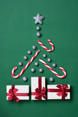 Christmas tree concept with gift boxes, candy canes, glitter globules and silver star on green background