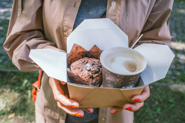 girl holding a box with a cupcake and coffee, street food
