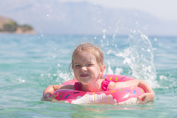 Fototapeta na wymiar happy little girl is swimming in an inflatable circle in the sea