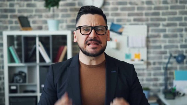 Portrait of angry bearded guy shouting and pointing at camera expressing anger standing alone in office. People, negative emotions and conflict concept.