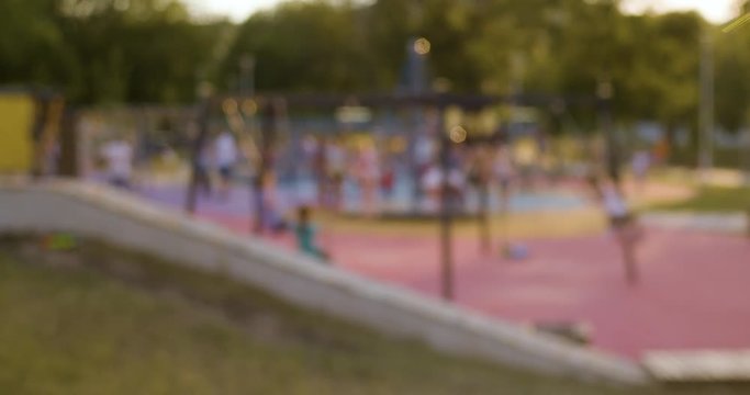 Blurred, out of focus shot of kids swinging on the playground. City life background, lens flare, Slow motion
