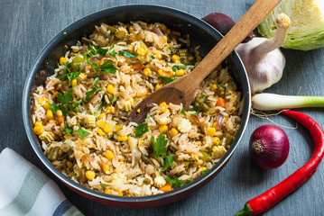 Fried rice with vegetables, in a pan and ingredients for cooking on a wooden table, top view, rustic style - a dish of Indian and Asian cuisine