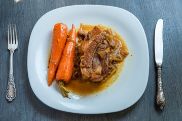 Fried pork belly with carrots and onion sauce on a plate, top view - french cuisine