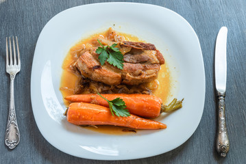 Fried pork belly with carrots and onion sauce on a plate, top view - french cuisine