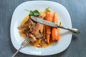Fried pork belly with carrots and onion sauce on a plate, top view - french cuisine