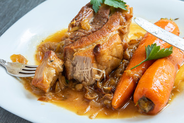 Fried pork belly with carrots and onion sauce on a plate close-up, top view - French, European cuisine