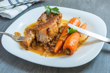 Fried pork belly with carrots and onion sauce on a plate close-up, top view - French, European cuisine