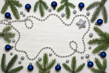 Christmas card concept with fir tree branches, blue baubles, one brocade star, brocade globules and silver bead chain on white wooden background - text space
