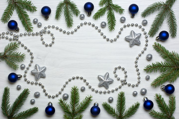 Christmas card concept with fir tree branches, blue baubles, brocade stars, brocade globules and silver bead chain on white wooden background - text space