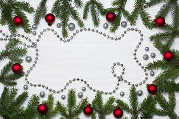 Christmas card concept with fir tree branches, red baubles, brocade globules and silver bead chain on white wooden background - text space