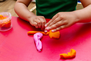 improving fine motor skills educational games concept, modeling soft clay plasticine children's hands close-up red background