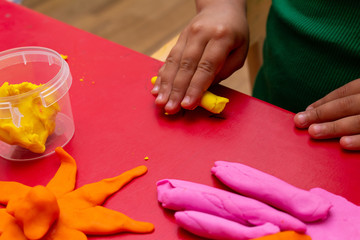 improving fine motor skills educational games concept, modeling soft clay plasticine children's hands close-up red background