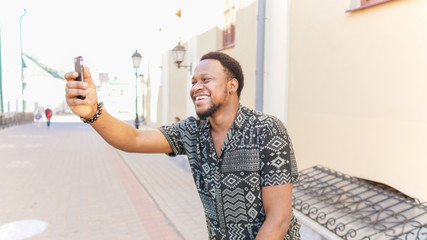 African cheerful man holding camera in hands and make a selfie outdoors.
