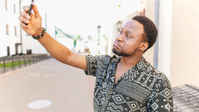 surprised african young man holding camera in hands and make a selfie outdoors.