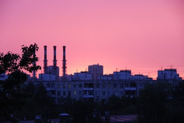 Pink sunset. roofs of multi-storey buildings, trees and pipes of the plant, the city Skyline at sunset, selective focus