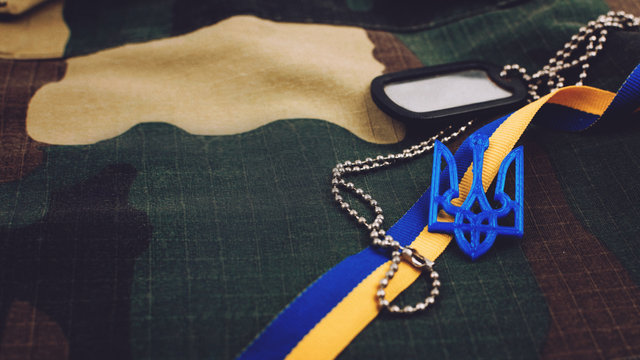 Ukraine military background . Ukrainian national symbols, Coat of arms trident, yellow and blue ribbon, army token on military uniform background