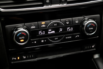 Сlose-up of the car  black interior:  dashboard with temperature, clock, adjustment of the blower, air conditioner and other buttons. Soft focus