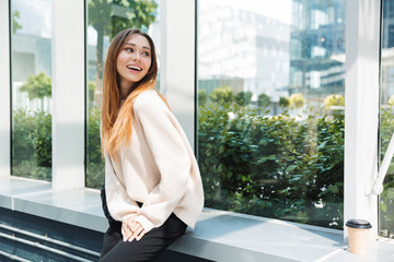 Photo of caucasian lovely woman smiling and looking aside while sitting near window in building...