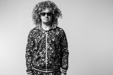 Adult pensive man posing om white studio background. Stylish funky male with curly hair black and white portrait. Confident guy in tracksuit expressing feelings. Unusual serious person in sunglasses.