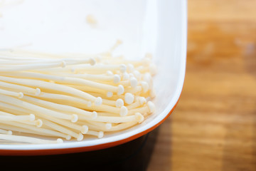 Close up fresh enoki mushroom or golden needle mushroom stacked on plate for shabu, BBQ grill in Korean or Japanese restuarant. Preparing raw materials for cooking concept. Flammulina velutipes.