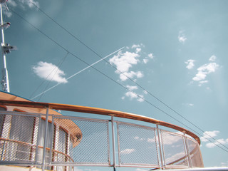 Upper deck of a cruise ship. Fencing - wooden handrails and metal mesh. Mast, windows. Clear day.