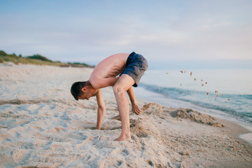 Man on the beach digging hole in sand beyond the sea in summer.