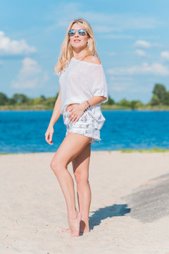 Beautiful nice blonde girl wear white tunic, shorts and baseball cap at the beach, summer fashionable concept 