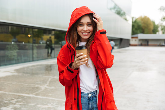Beautiful excited emotional young happy pretty woman in raincoat posing outdoors drinking coffee.