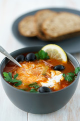 Meat solyanka served with rye bread in a grey ceramic bowl. White wooden table, high resolution