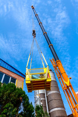 Fototapeta premium Mobile crane with hook and straps is raising work platform, basket
