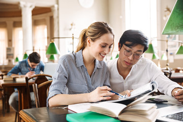 Fototapeta premium Smart cheerful teenagers studying at the library together