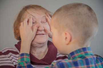 Elderly grandmother and grandson spend time together in green checkered shirt. Boy and the old woman are very attached to each other.