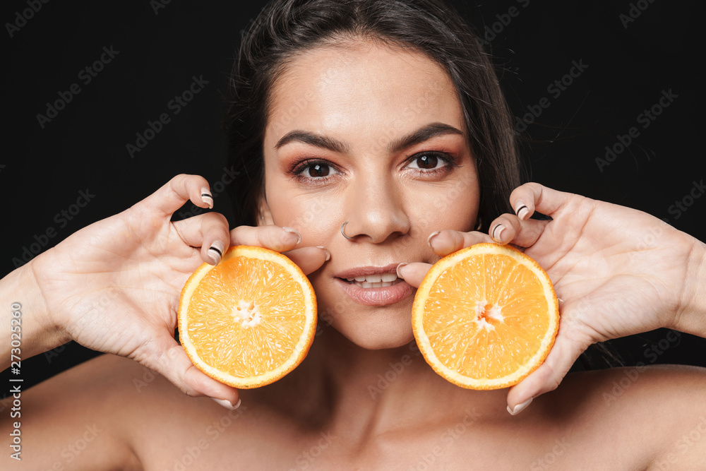 Sticker Beautiful naked woman posing isolated over black wall background holding orange citrus.