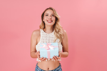 Fototapeta na wymiar Happy young woman posing isolated over pink wall background holding present box.