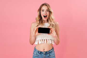 Happy young woman posing isolated over pink wall background using mobile phone.