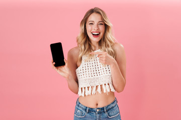 Happy young woman posing isolated over pink wall background using mobile phone.