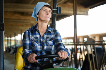 Mature female worker in tractor on farm