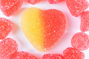 Red jelly sweets around a large red-yellow heart-shaped candy close-up on a light background. The concept of bright sweets, harmful delicacy.