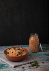 salad of fermented cabbage and cranberries with parsley in a clay cup and a glass jar with cabbage on a wooden table on a black background