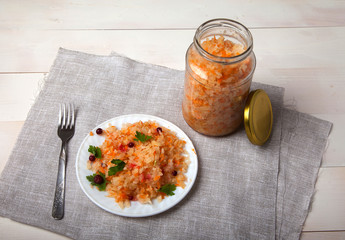 fermented cabbage in a glass jar and a plate with cabbage and cranberries on a white table