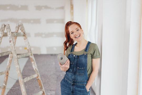 gl&uuml;ckliche frau auf der baustelle mit einer rolle tapete unter dem arm
