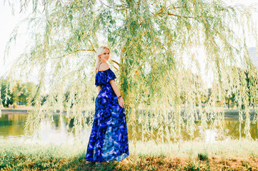 Beautiful blonde girl posing at nature in blue dress