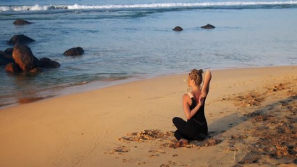 tremendous lady in black tracksuit sits in yoga pose on sandy beach near ocean backside view extreme slow motion. Concept spiritual practices