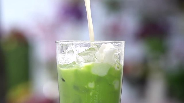 close up Pour milk into a glass of green ice tea,  Slow motion shot