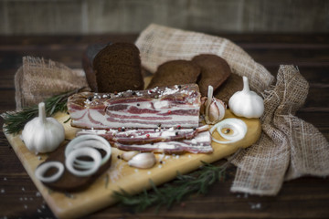 Pork salted lard with bread, garlic and onion on a dark wooden background in a rustic style.