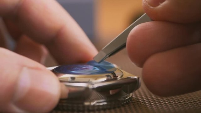 Close-up of the man's hand, removing with tweezers protective sticker with a new watch. Unpacking a new watch.