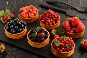 Fruit and berry tartlets dessert tray assorted . Beautiful delicious tarts, bright, colorful pastry cakes sweets with fresh raspberries, figs, strawberry. on dark wooden background