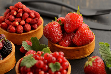 Fruit and berry tartlets dessert tray assorted . Beautiful delicious tarts, bright, colorful pastry cakes sweets with fresh raspberries, figs, strawberry. on dark wooden background