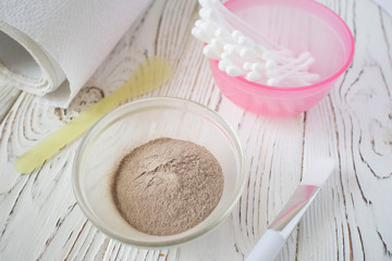 bowl with cosmetic dirt, skin care kit ha, brush, cotton sticks on wooden background