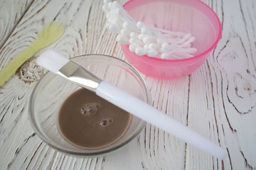 bowl with cosmetic dirt, skin care kit ha, brush, cotton sticks on wooden background